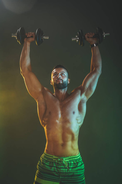 Concentrated handsome muscular man is training actively and hard with dumbbells. - Foto, imagen