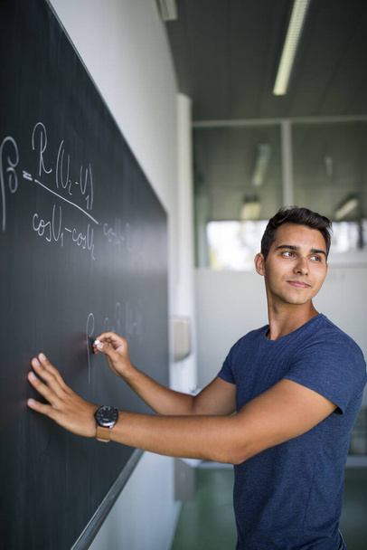 Students in a classroom - handsome student solving a math problem on a blackboard during math class - Fotografie, Obrázek