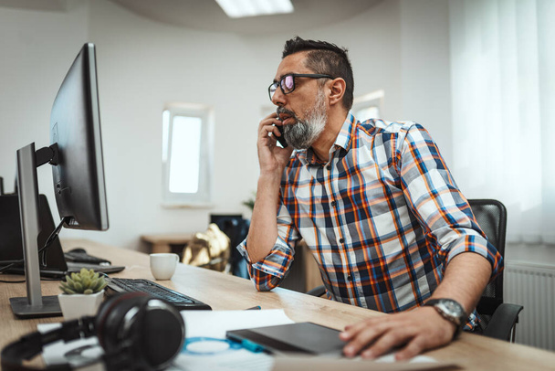 Hezký úspěšný podnikatel mluví na mobilu, zatímco pracuje v kanceláři. - Fotografie, Obrázek
