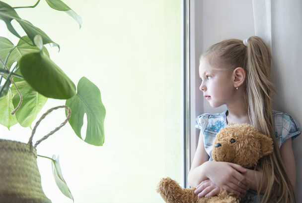 Sad child girl  by the window at home. Quarantine. Coronavirus pandemic. Stay home concept. - Photo, Image