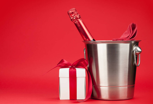 Butelka szampana w wiadrze na lód i Walentynki lub pudełko świąteczne przed czerwonym tle z miejscem na pozdrowienia  - Zdjęcie, obraz