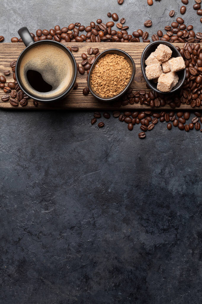 Koffiekopje, suiker en geroosterde bonen op donkere stenen tafel. Bovenaanzicht met kopieerruimte. Vlakke plaat - Foto, afbeelding