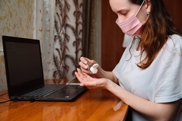 Coronavirus lockdown. woman working from home with mask in quarantine. Close-up of hands with sanitizer gel. - Фото, зображення