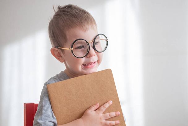 Little cute toddler preschooler boy in glasses with book looking straight at camera. Back to school concept - Фото, зображення