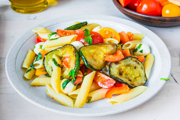 Margarita pasta in a plate on a wooden table - penne with tomatoes, zucchini, mozzarella and basil - 写真・画像