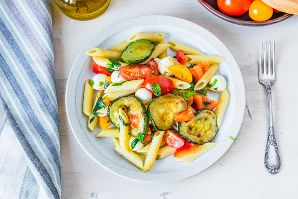 Margarita pasta in a plate on a wooden table - penne with tomatoes, zucchini, mozzarella and basil - Photo, Image