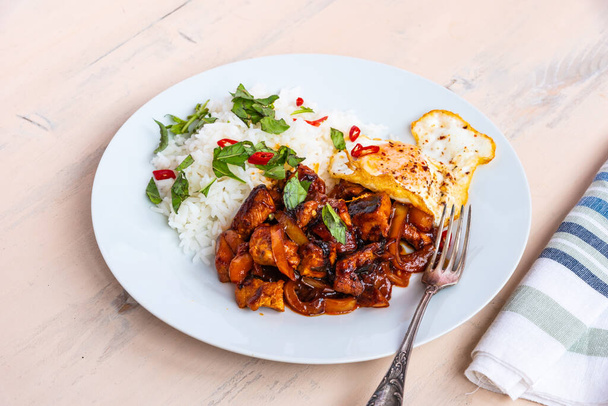 Cucina tailandese - basilico tailandese di pollo, pollo in salsa con riso e uovo fritto, su un piatto su un tavolo rustico leggero
 - Foto, immagini