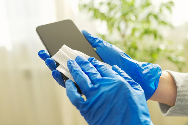Close up of hands in rubber gloves disinfecting mobile phone - Foto, imagen