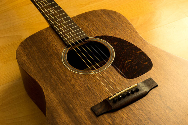 Egy barna fából készült gitár a padlón, oldalról meleg fénnyel. - Fotó, kép