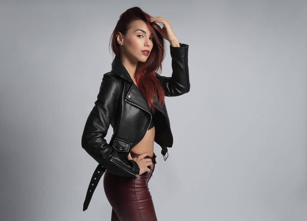fashion shoot with red haired woman in leather jacket, red leather pants - Zdjęcie, obraz