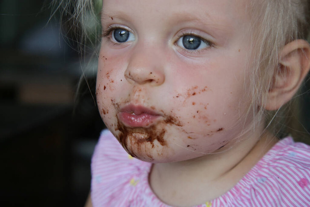 Candid portrait of a toddler girl eating chocolate cake. Happy childhood concept. - Photo, Image