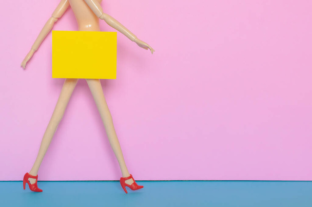Naked female doll walking with red shoe with yellow paper hiding the bottom area. Minimal beauty and sexually harassment concept. - Photo, Image
