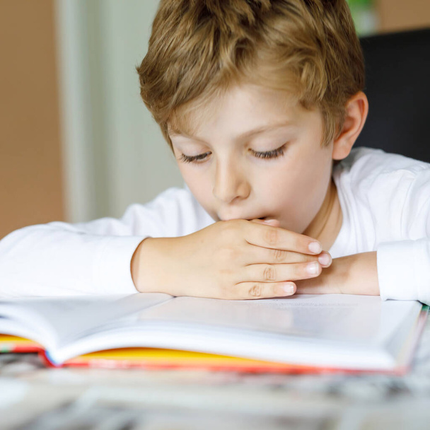 コロナ大流行病からの隔離期間中に宿題をする勤勉な幸せな学校の少年。ペンで健康的な子供の書き込み、自宅に滞在。家庭教育の概念 - 写真・画像