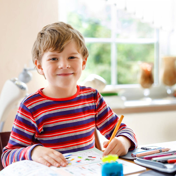 コロナ大流行病からの隔離期間中に宿題をする勤勉な幸せな学校の少年。ペンで健康的な子供の書き込み、自宅に滞在。家庭教育の概念 - 写真・画像