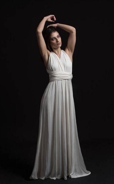 όμορφο μοντέλο κάνει μια εικονογραφική φωτογράφιση σαν μια ελληνική θεά με μαύρο φόντο - Φωτογραφία, εικόνα