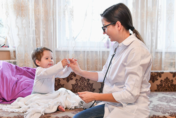 Ο γιατρός δίνει βιταμίνες στο παιδί. Γυναίκα γιατρός στο σπίτι. ο παιδίατρος δίνει βιταμίνες σε μικρό ασθενή μετά την εξέταση. - Φωτογραφία, εικόνα