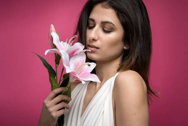 nice look of a woman with flowers and pink background and smell flowers - Photo, Image