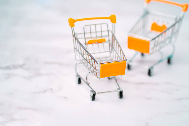 Two empty small miniature toy shopping trolley on light background. Selective focus. Shopping, purchases, supermarket, sale concept. - Фото, зображення