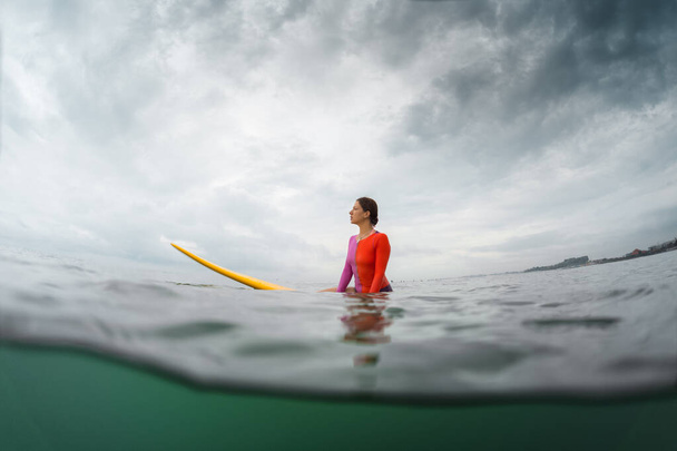 Underwater split shot of the young lady surfer sitting on a board awaiting the waves - Foto, immagini