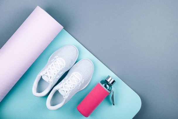 Bovenaanzicht van witte sportschoenen sneakers blauw roze yoga mat, glazen waterfles op pastelgrijze achtergrond. Yoga pilates of fitness training. Afvallen en sport concept. Platte laag. - Foto, afbeelding