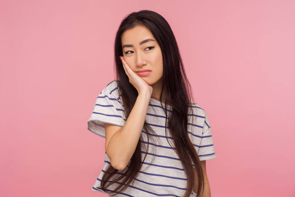 Portrait of bored lazy upset girl with brunette hair leaning on hand and looking with gloomy indifferent expression, listening to boring tedious talk. indoor studio shot isolated on pink background - 写真・画像