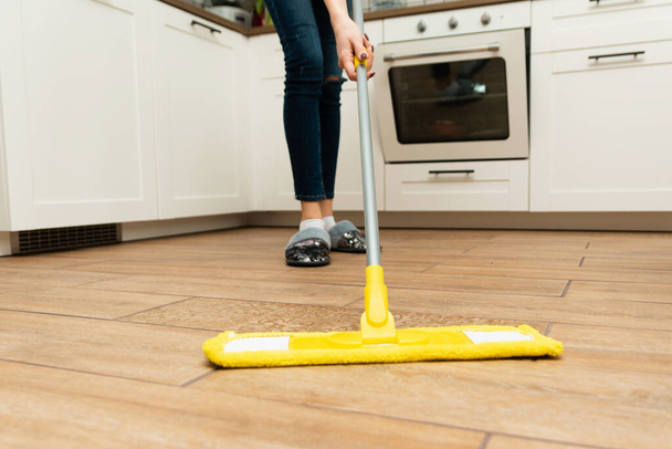 主婦が家で掃除する価値がある。素敵な女性は明るいキッチンでラミネートから木製の床を洗う. - 写真・画像