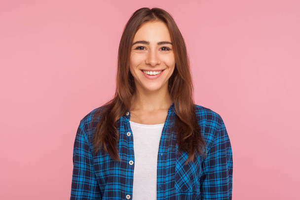 Portrait of friendly good-natured girl in checkered shirt smiling sincerely at camera, looking satisfied contented with life, rejoicing positive news. indoor studio shot isolated on pink background - Foto, immagini