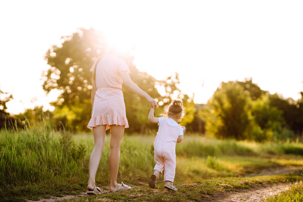 Μητέρα και μικρή κόρη παίζουν μαζί σε ένα καλοκαιρινό πάρκο το ηλιοβασίλεμα. Ευτυχισμένη μαμά με μικρό παιδί που διασκεδάζει στο ηλιόλουστο γήπεδο. Φιλιά και αγκαλιές. Η έννοια της ευτυχισμένης οικογένειας.  - Φωτογραφία, εικόνα