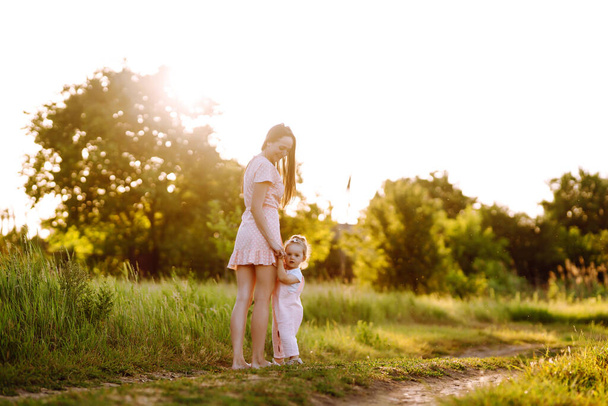 Matka a dceruška si spolu hrají v letním parku při západu slunce. Šťastná máma s malým dítětem baví na slunečném poli. Líbání a objímání. Koncept šťastné rodiny.  - Fotografie, Obrázek
