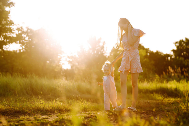 Mother and little daughter playing together in a summer park at sunset. Happy mom with small child  having fun on sunny field. Kisses and hugs. The concept of a happy family.  - Φωτογραφία, εικόνα