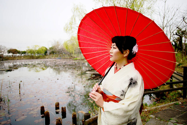 Portrait of Japanese woman wearing white kimono holds a red umbrella at park in Tokyo, Japan. - Photo, Image