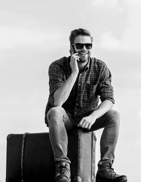 Travel blogger. Man sit on suitcase before journey. Business trip. Handsome guy traveler. Guy outdoors with vintage suitcase. Luggage concept. Calling taxi. Travel agency. Travel with luggage - Fotografie, Obrázek