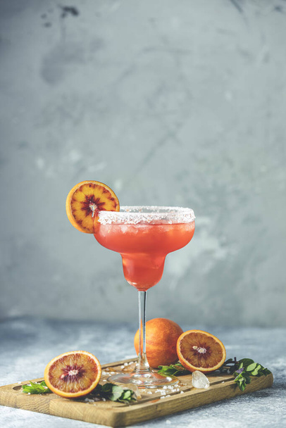Красный апельсиновый коктейль маргариты с текилой, тройной секундой, апельсиновым соком, дробленым льдом и солью на краю стакана, украшенный цитрусовым ломтиком Мелкая глубина поля, светлый каменный фон
 - Фото, изображение