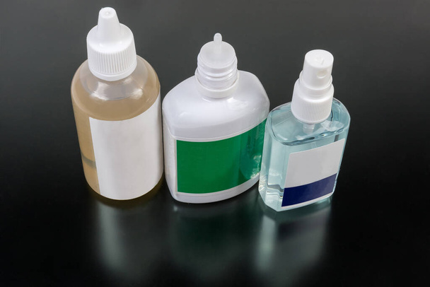 Petites bouteilles en plastique des différents antiseptiques sur une surface mate foncée
 - Photo, image