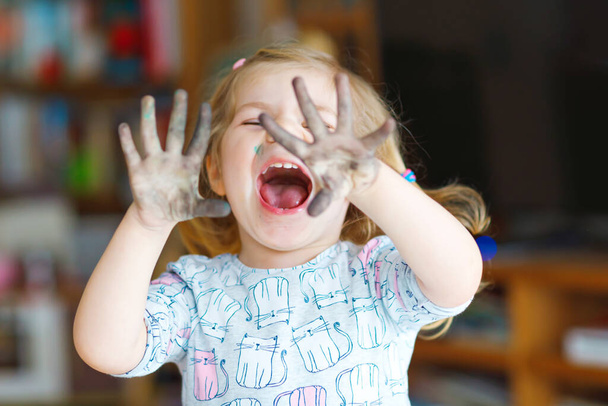 Söpö suloinen vauva tyttö oppimisen maalaus vesiväreillä. Pieni lapsi piirustus kotona, käyttäen värikkäitä harjat. Terve onnellinen lapsi, jolla on likaiset kasvot ja kädet kotona tai lastentarhassa - Valokuva, kuva