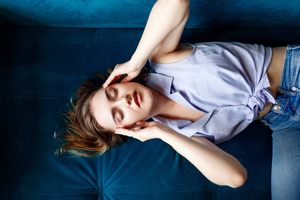 Mujer joven acostada en el sofá y sufriendo de dolor de cabeza en casa
. - Foto, imagen