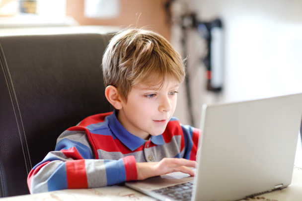 Egy kisiskolás, aki iskolai házi feladatot csinál a számítógépen. Gyerek tanulás a PC-n. Keményen dolgozó fiú gyakorol a karantén ideje alatt a corona világjárvány miatt. Otthoni tanulás koncepciója. - Fotó, kép