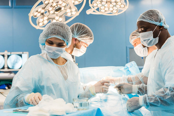 An international team of doctors performs a complex surgical operation on a patient under anesthesia. Modern operating room and experienced surgeons save lives - Foto, Imagem