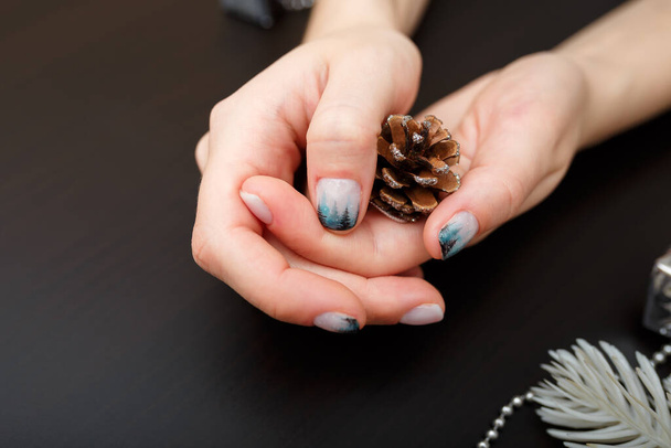 Mãos femininas com manicure de floresta de abeto que mantém o cone de pinheiro no fundo preto. Arte de Natal ou de Inverno. Mãos cuidado, design de unhas, beleza e conceito de saúde. Espaço de cópia. - Foto, Imagem