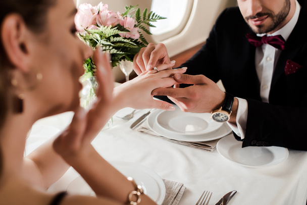 selective focus of man putting wedding ring on finger on surprised woman while making marriage proposal in plane - Photo, Image