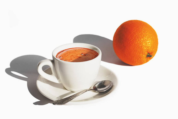 Taza blanca de café y una naranja sobre fondo blanco con duras sombras de luz de la mañana. Mejor comienzo del día. Copiar espacio
 - Foto, Imagen