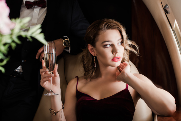 cropped view of man standing near pensive, beautiful woman holding glass of champagne in plane - Fotografie, Obrázek