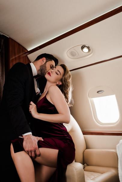 элегантный мужчина касается ноги и целует страстную женщину в самолете
 - Фото, изображение