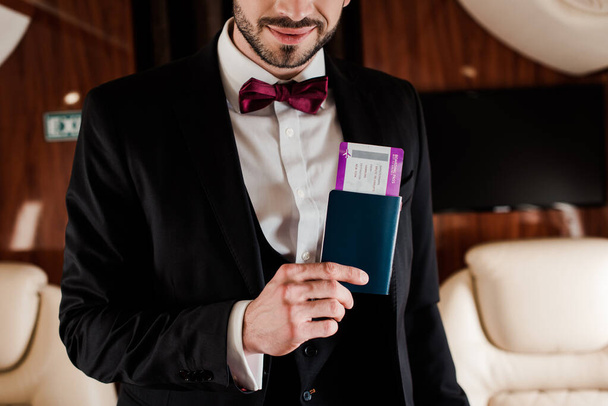 cropped view of elegant man holding passport and air ticket in plane - Photo, Image