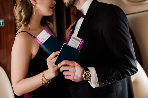 обрізаний вид елегантної пари, що тримає паспорт та авіаквиток у літаку
 - Фото, зображення