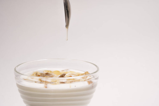 Honey pours from a spoon into a delicious and healthy breakfast in a glass. Greek yogurt with granola and honey on a white background - Foto, imagen