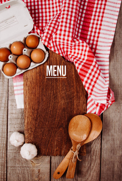 Houten snijplank op een houten ondergrond met knoflook, pollepels en eieren met offerte Recept - Foto, afbeelding