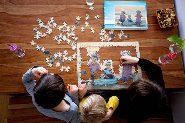 Three children, boys, assembling puzzle with their picture from the beach, playing at home together - Fotó, kép