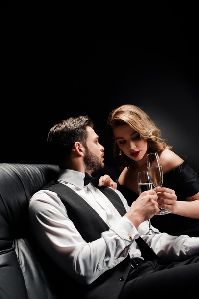donna attraente ed elegante uomo clinking bicchieri di champagne mentre seduto sul divano in pelle su sfondo nero
 - Foto, immagini