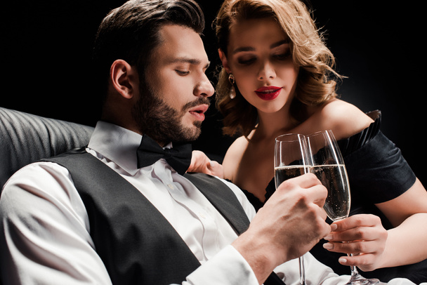 atractiva mujer y elegante hombre tintineo copas de champán aislado en negro
 - Foto, Imagen